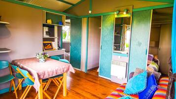 A cozy room with a wooden floor, a dining table with chairs, a sofa with colorful cushions, and a kitchenette area.