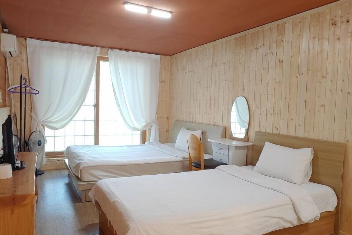 Een kamer met twee bedden, een bureau, een spiegel en een raam met gordijnen.