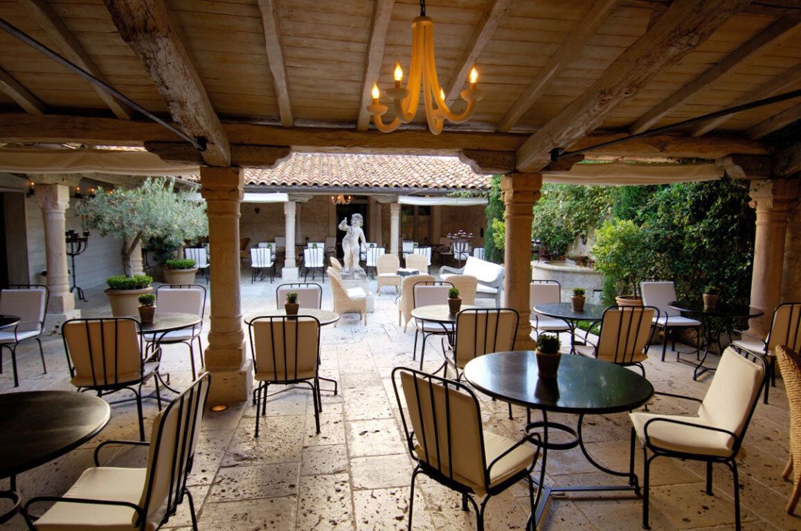 An outdoor patio with round tables and chairs, a statue, and a tiled roof structure.