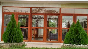 A modern building with large glass doors, a wooden balcony, and two potted evergreen trees in the foreground. - Hotel Bundala Park - Hostel (Lunugamvehera)