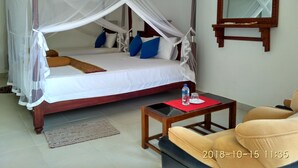 A room with a four-poster bed, a wooden nightstand, a red mat, a glass table, and a chair. - Hotel Bundala Park - Hostel (Lunugamvehera)