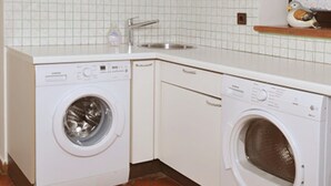 Une cuisine compacte avec deux lave-linge blancs, un pare-feu en carrelage et une fenêtre avec un rideau.
