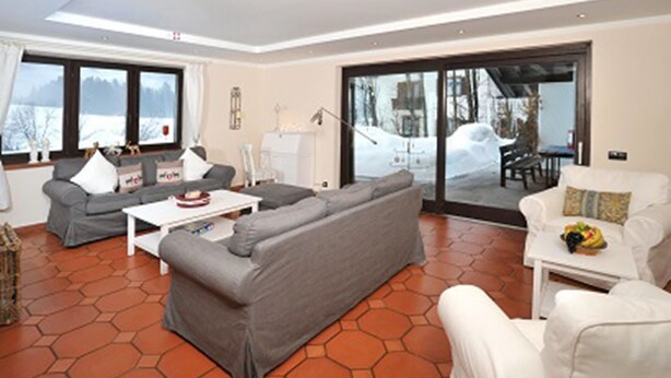 Un salon moderne avec un canapé gris, des fauteuils blancs et une table basse. De grandes fenêtres offrent une vue sur un paysage enneigé.
