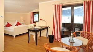 Une chambre d’hôtel avec un lit, un bureau, une chaise, une table et une vue sur un paysage enneigé, visible à travers de grandes fenêtres.