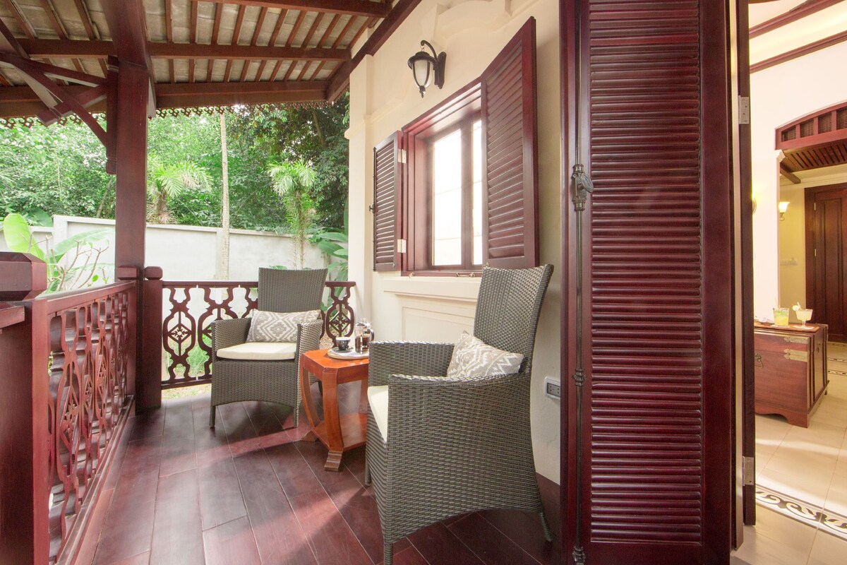 A covered outdoor seating area with wicker chairs and a small table, a window with shutters, and a door leading to an interior space.