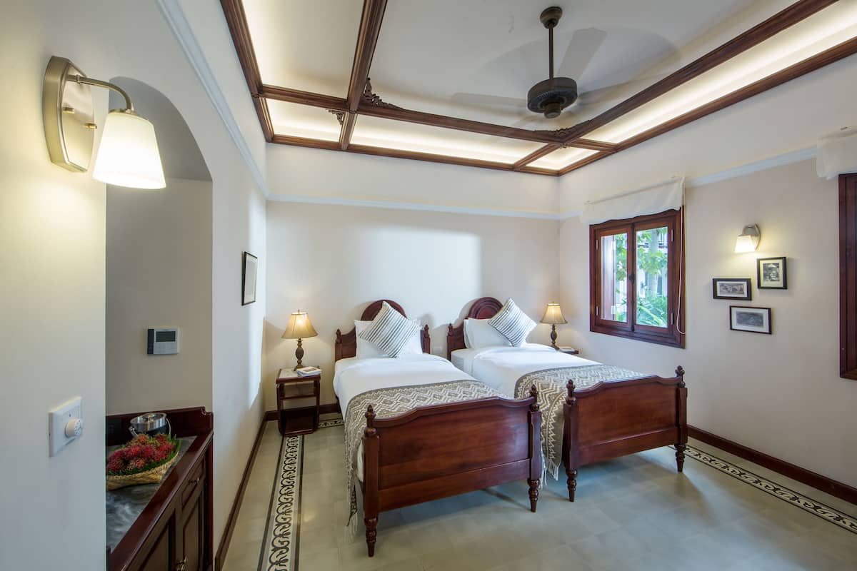 A bedroom with two wooden beds, a ceiling fan, and a window with curtains.