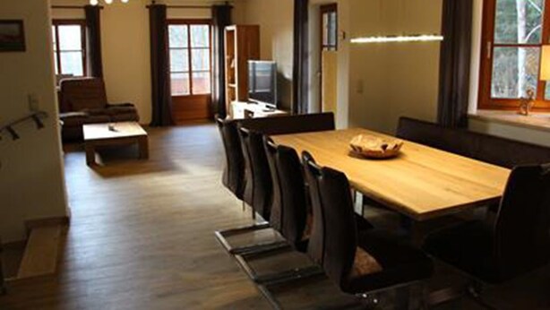 A dining area with a long wooden table and chairs, a television, and a window with curtains. - Ferienhaus Thimlefi (Reit im Winkl)