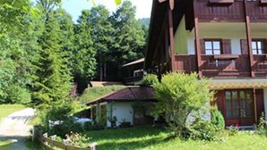 A traditional wooden chalet with a balcony, surrounded by lush greenery and a paved path. - Ferienhaus Thimlefi (Reit im Winkl)