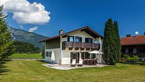 Ein zweistöckiges Haus mit Balkon, Rasen und einem Berg im Hintergrund.