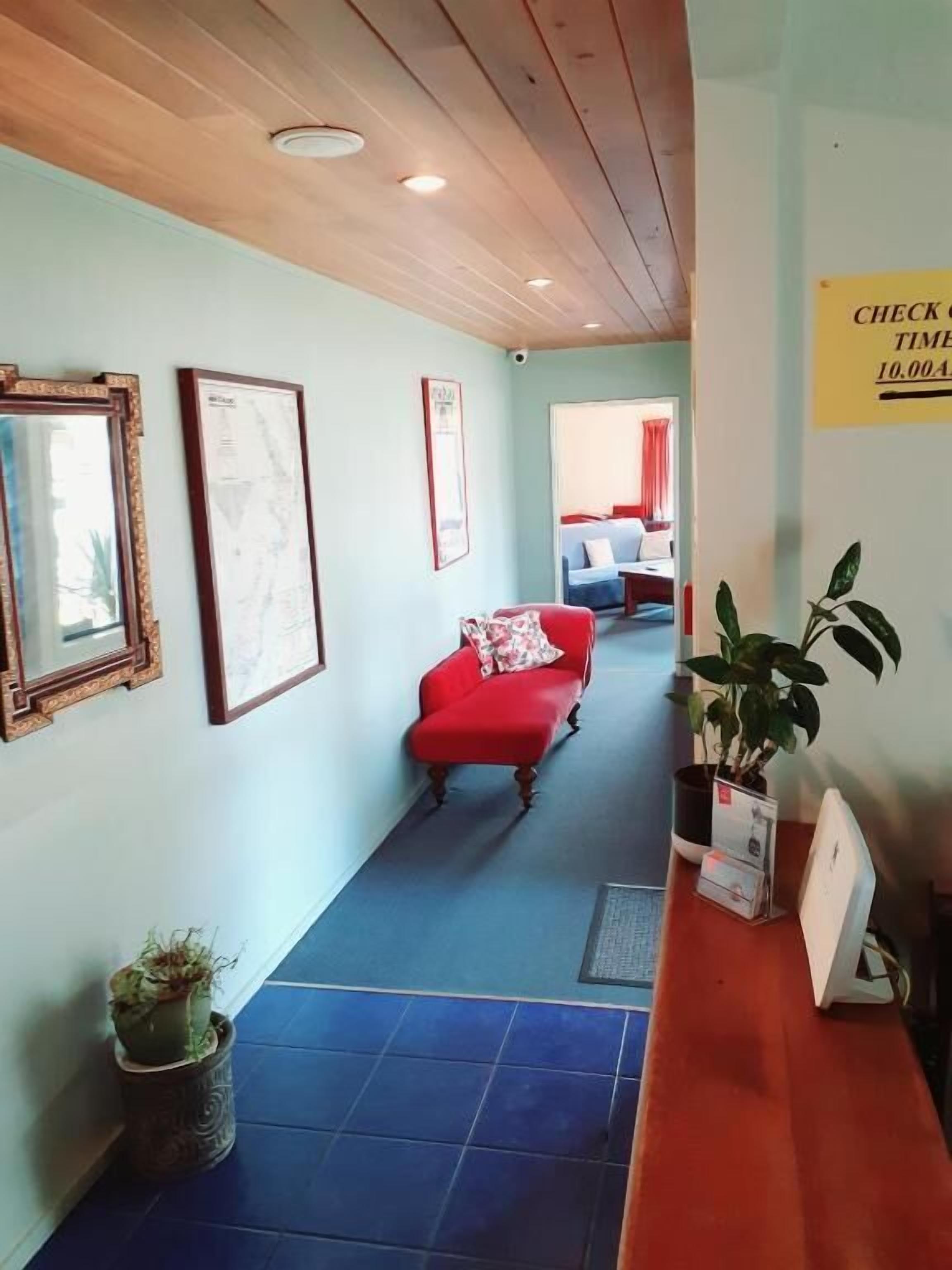 A hallway with a red sofa, framed pictures on the walls, a check-in time sign, and a potted plant.