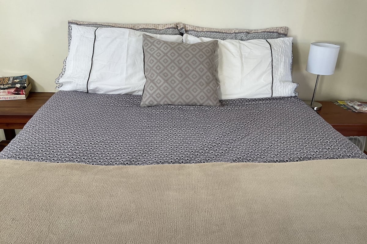 A neatly made bed with patterned bedding, a bedside table with a lamp, and a small stack of books.