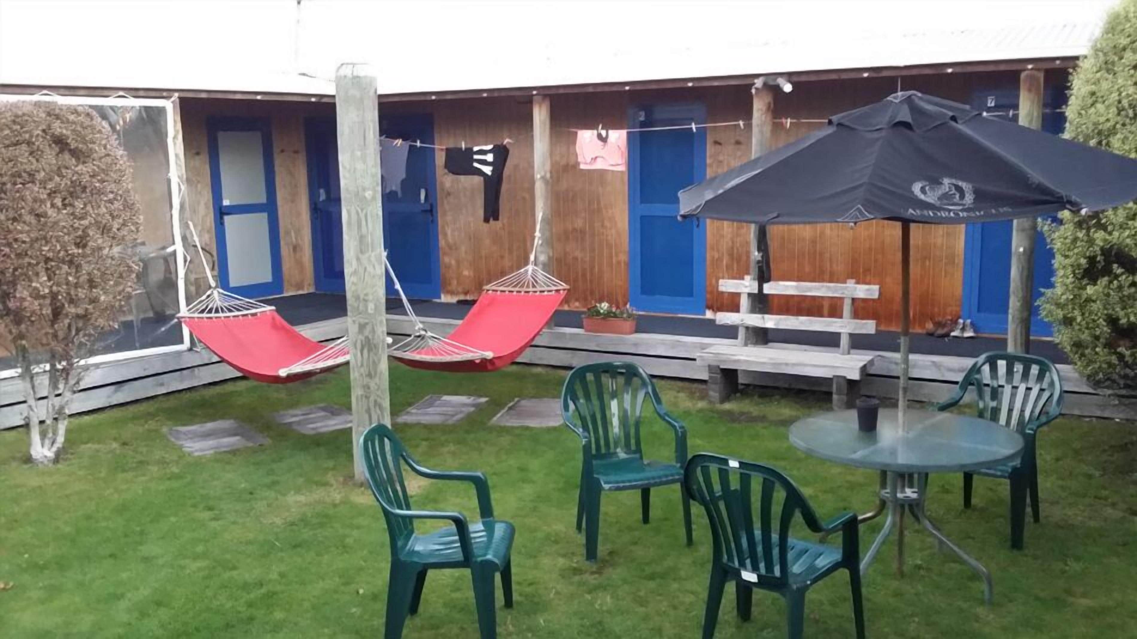 Un espace patio avec des chaises vertes, une table ronde et deux hamacs rouges.
