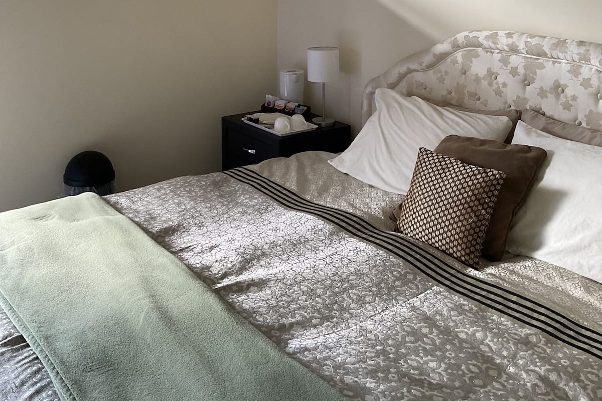 A neatly made bed with patterned bedding, a bedside table with a lamp, and a window with curtains.