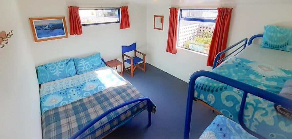Een kamer met twee bedden, een stoel en twee ramen met rode gordijnen.