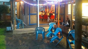 An outdoor patio area with blue plastic chairs and tables, string lights, and a wooden fence. - Tongariro River Retreat - Hostel (Turangi)