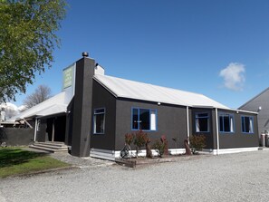A black building with blue-framed windows, a white roof, and a gravel driveway.