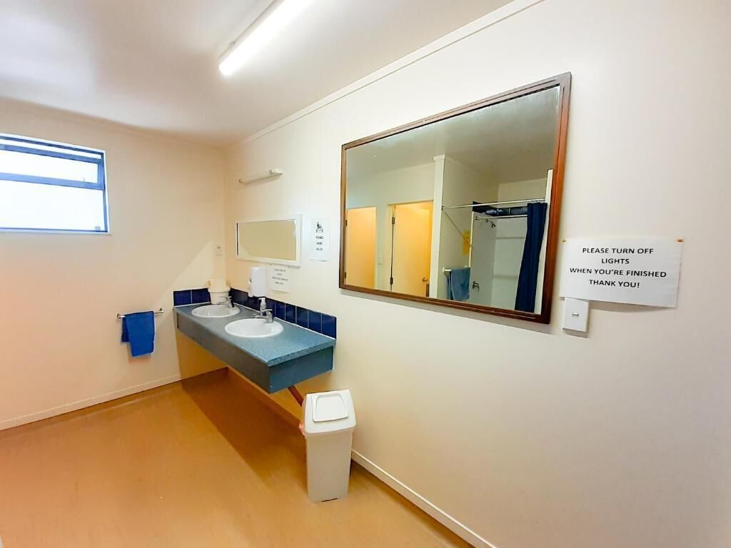 Un bagno con due lavandini, uno specchio, un cestino e un cartello che invita a spegnere le luci.