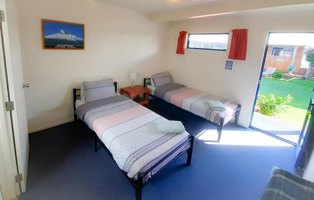 A room with two single beds, a small table, a chair, and a window with curtains.