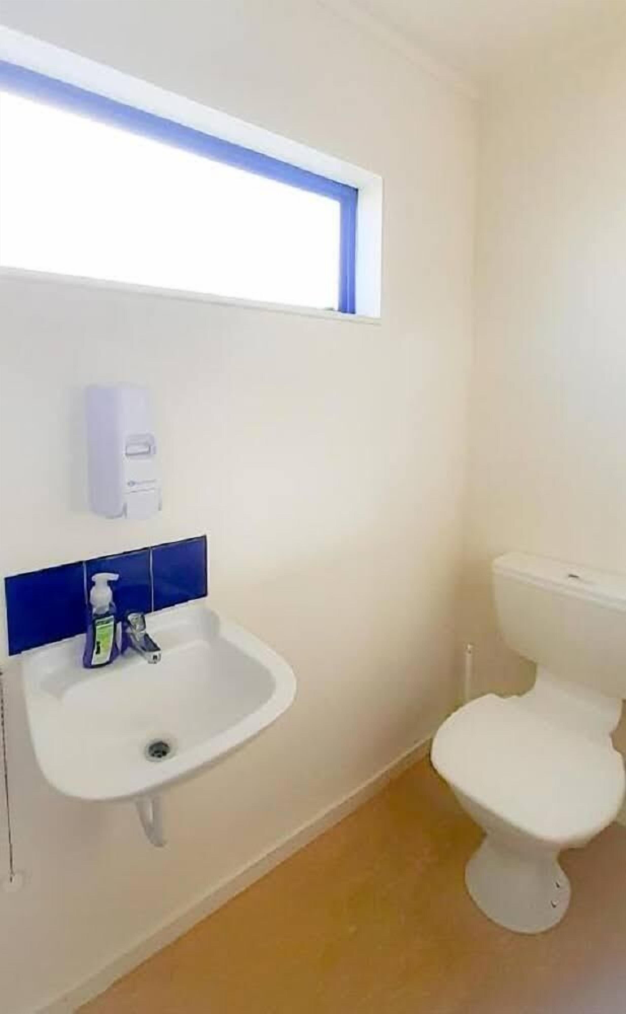A small bathroom with a white sink, a toilet, and a window above the sink.