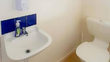 Une petite salle de bain avec un lavabo blanc, des toilettes et une fenêtre située au-dessus du lavabo.
