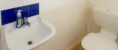 Un baño pequeño con un lavamanos blanco, un inodoro y una ventana sobre el lavamanos.
