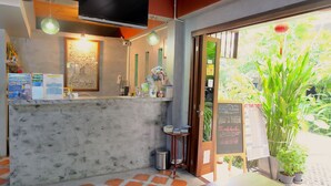 Un área de recepción con un mostrador de hormigón, un televisor montado en la parte superior y un cartel con un horario.