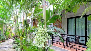 Un exuberante jardín interior con un sendero de piedra, un área de descanso con sillas y un edificio con grandes ventanales.