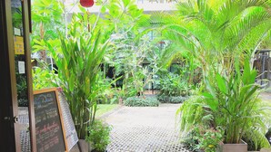 Un exuberante jardín interior con un pizarrón que muestra el horario de atención y la información de contacto.