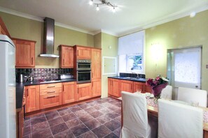 Une cuisine avec des meubles de rangement en bois, une cuisinière et un coin repas comprenant une table et des chaises.