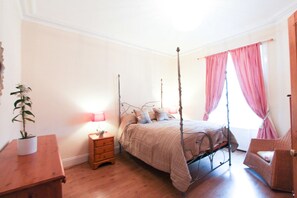 Une chambre à coucher avec un lit à baldaquin, une table de chevet avec une lampe, une commode en bois et une chaise.