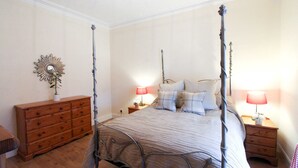 Un lit à baldaquin avec une structure en métal, une commode en bois dotée de nombreux tiroirs et deux tables de chevet avec des lampes.