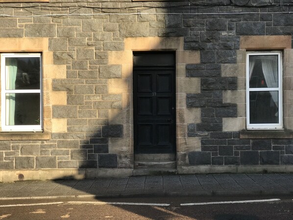 Un bâtiment en pierre avec une porte noire, deux fenêtres et le numéro « 37 » bien visible sur la porte.