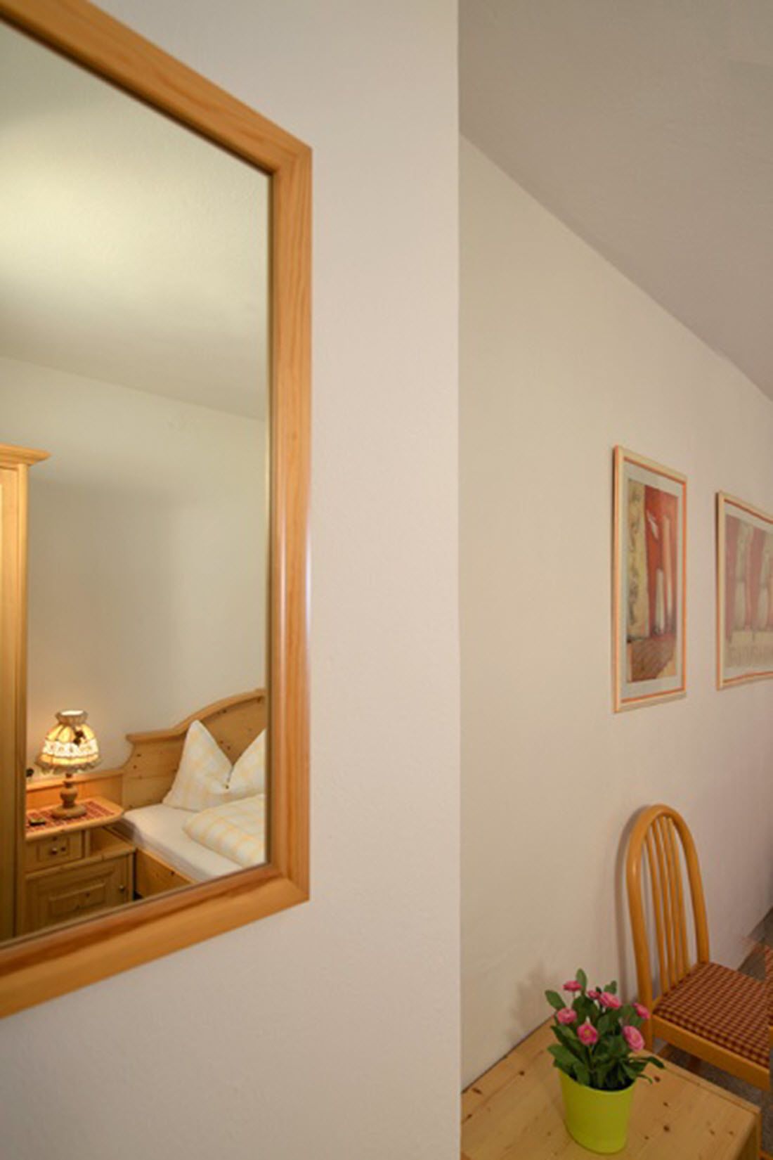 A bedroom with a wooden bed, a bedside table with a lamp, a chair, and a small table with a potted plant.