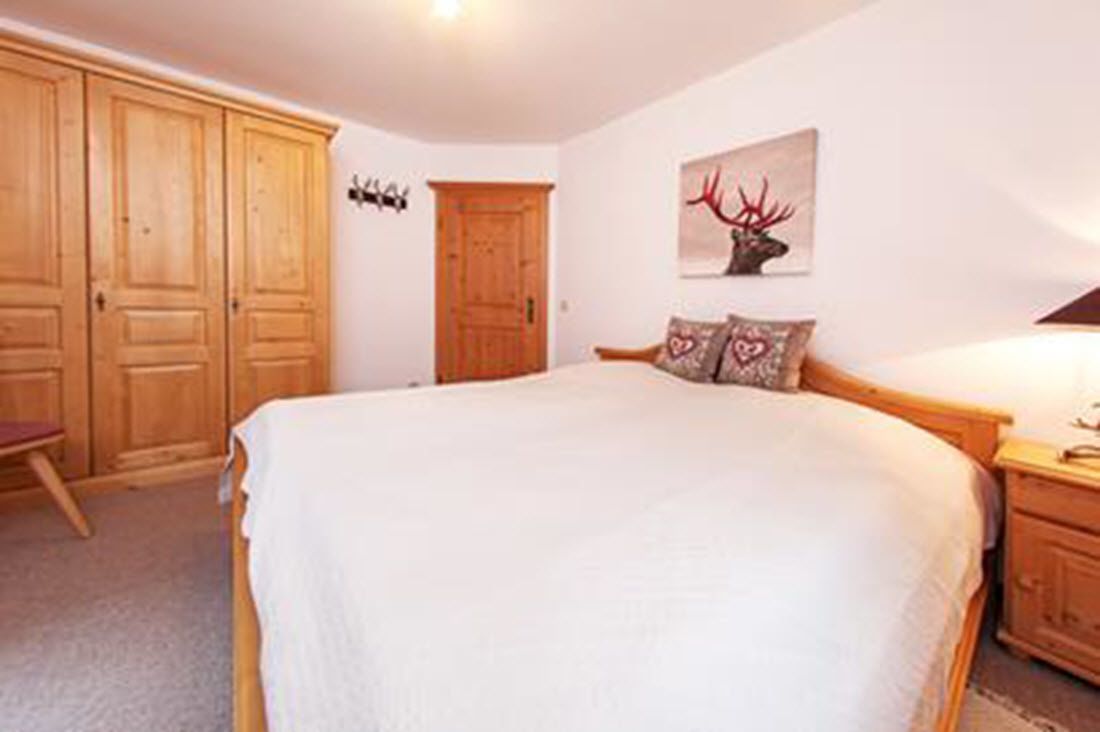 A bedroom with a large bed, wooden wardrobe, and a wall-mounted deer head decoration.