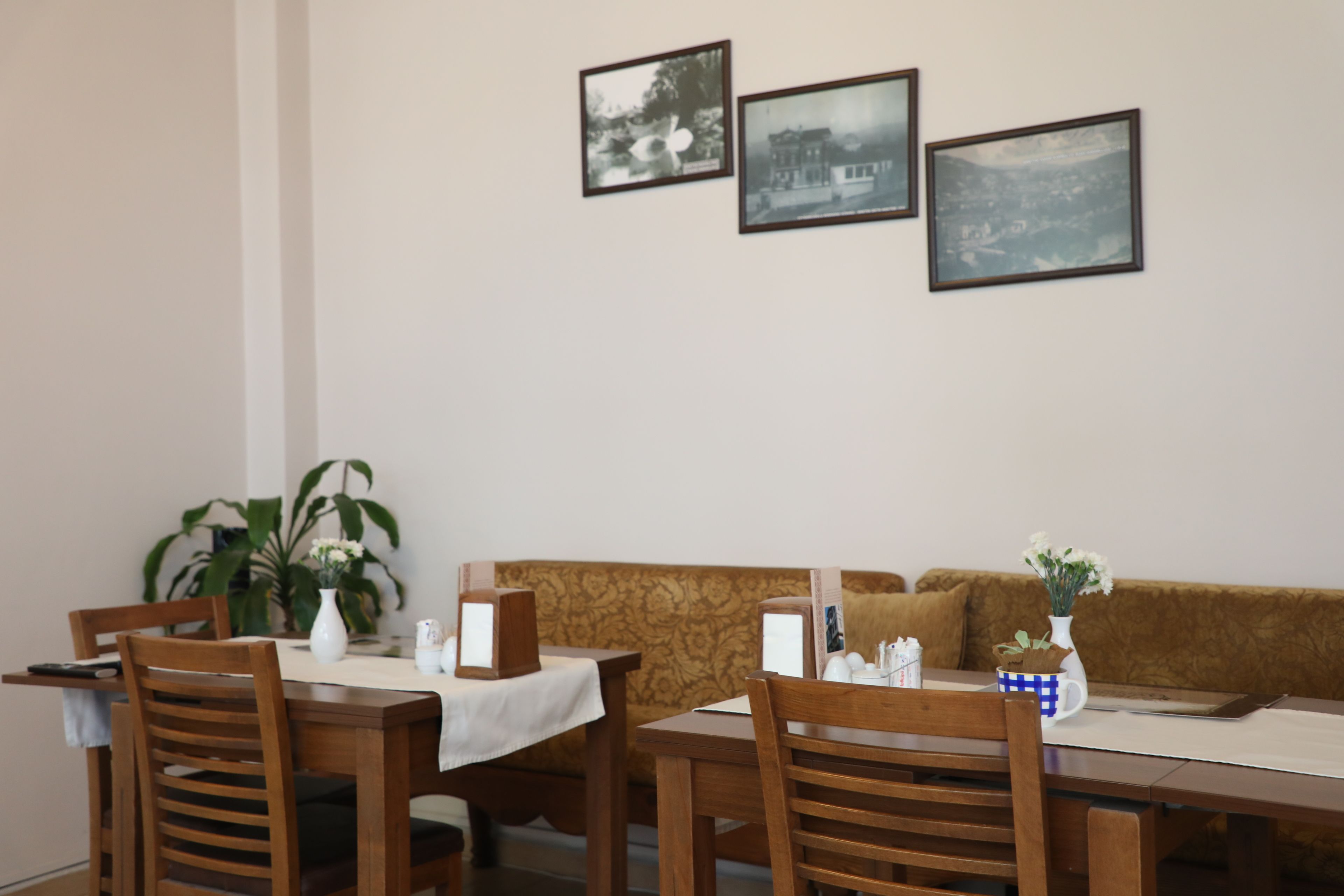 A dining area with wooden tables and chairs, a patterned sofa, and three framed pictures on the wall.