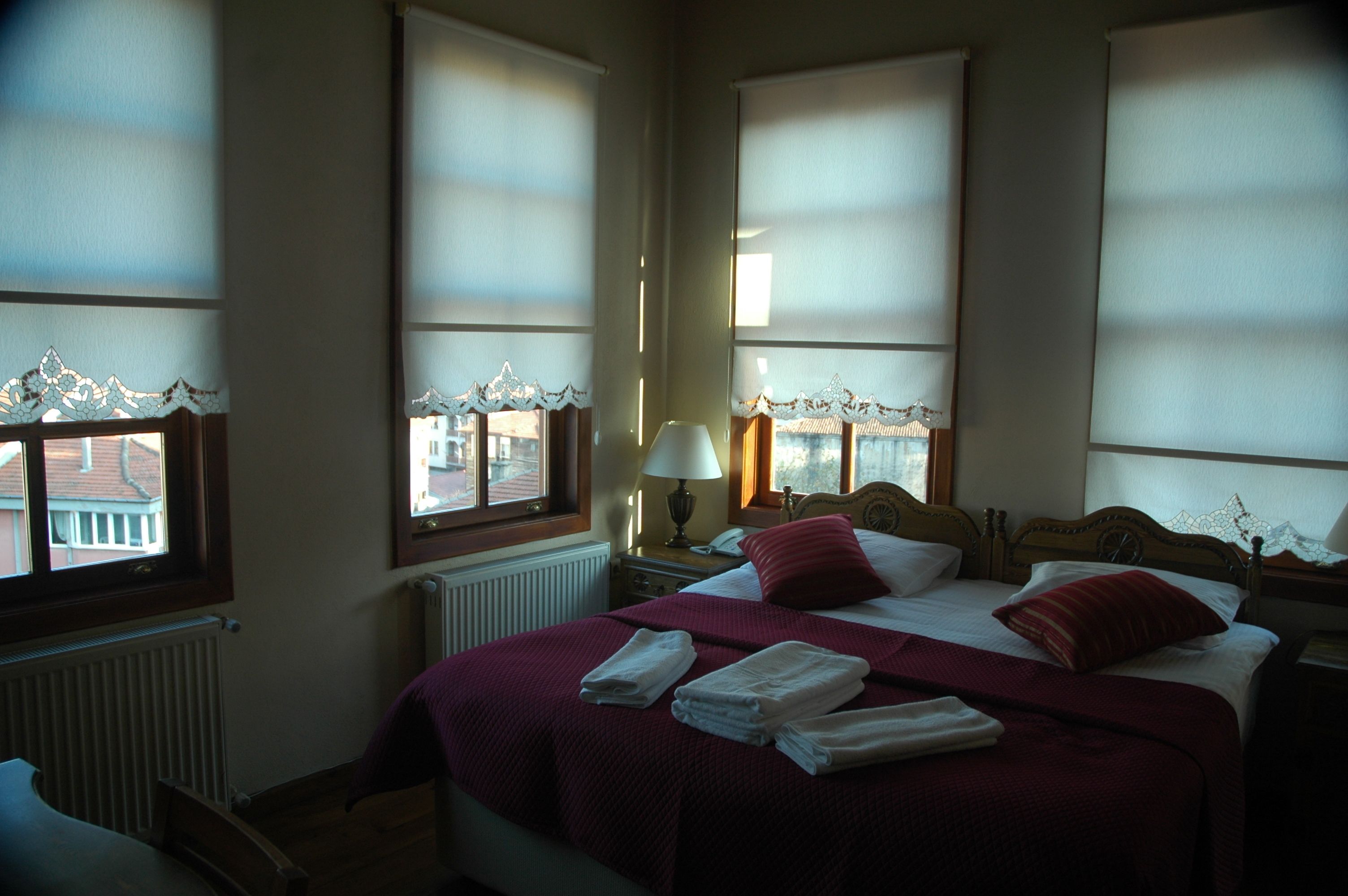 Une chambre d’hôtel avec un grand lit, deux tables de chevet, une petite table, une lampe et une vue par les fenêtres.