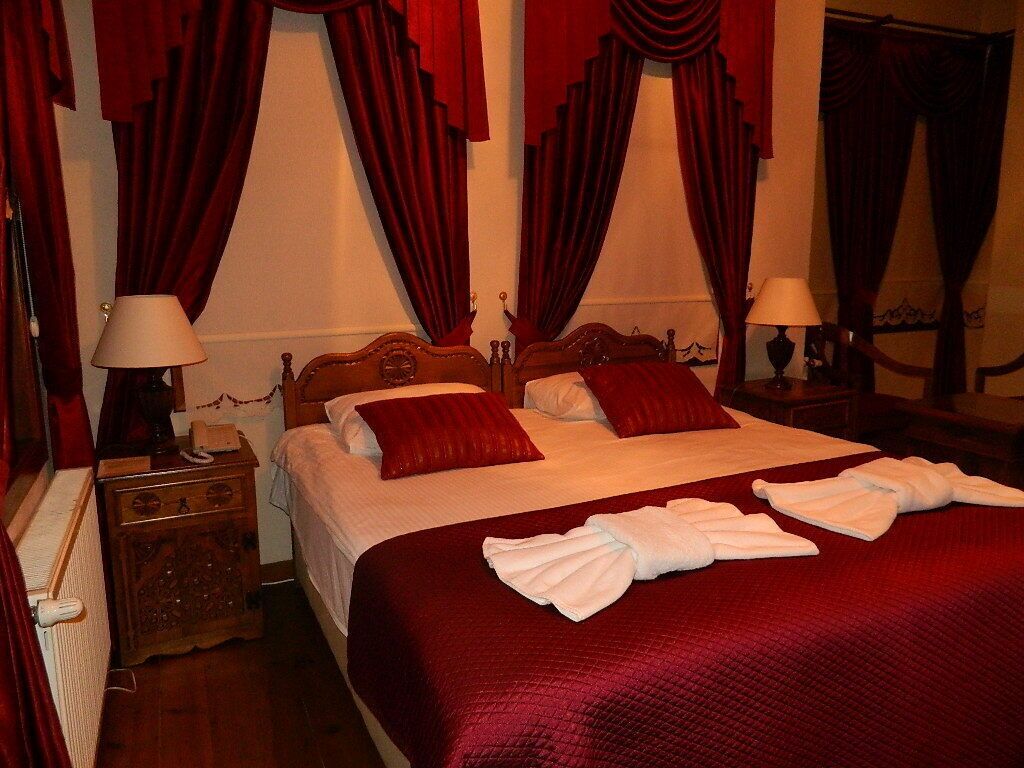 A hotel room with a large bed, red curtains, a wooden nightstand, and a lamp.