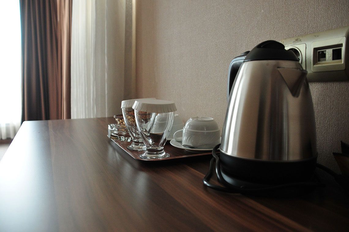 A wooden table with a coffee maker, four cups, and a tray.