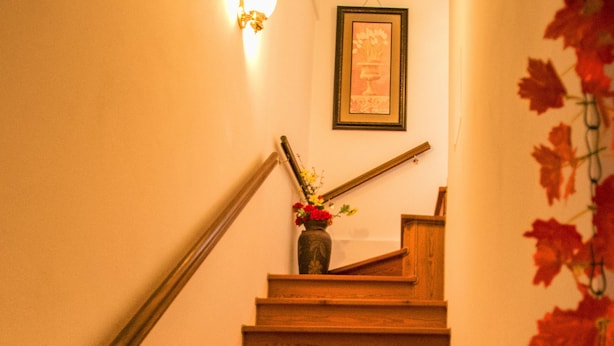 A wooden staircase with a handrail, a framed picture on the wall, and a vase with flowers at the top. - Chiaro Di Luna (San Vito al Tagliamento)