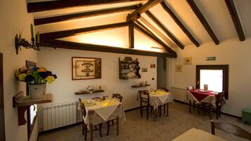 A dining area with wooden beams, tables with tablecloths, and a radiator.