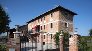 A multi-story brick building with a gated entrance, a red awning, and a staircase leading to the entrance. - Chiaro Di Luna (San Vito al Tagliamento)