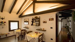 A dining area with wooden beams, a table set for two, and a potted plant in the hallway. - Chiaro Di Luna (San Vito al Tagliamento)