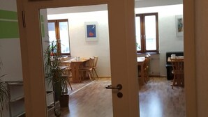 A room with a wooden floor, a door with a glass panel, and a view of a dining area with tables and chairs. - Gästehaus Ruh (Freiburg im Breisgau)