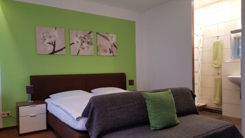 Un dormitorio con una cama, paredes verdes y tres cuadros florales.