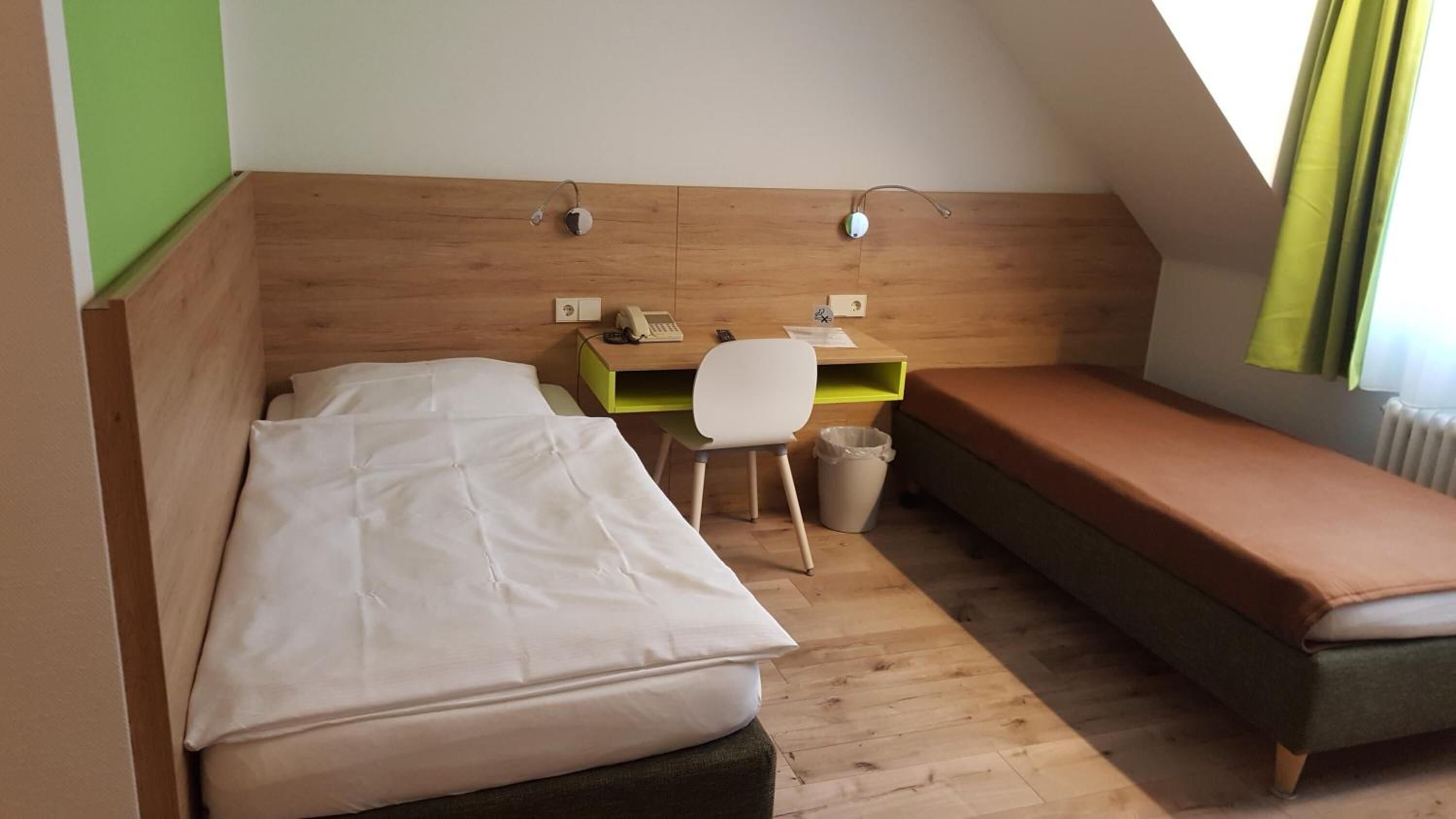 Eine kleine, einfache Unterkunft mit einem Bett, einem Schreibtisch, einem Stuhl und einer kleinen Couch.