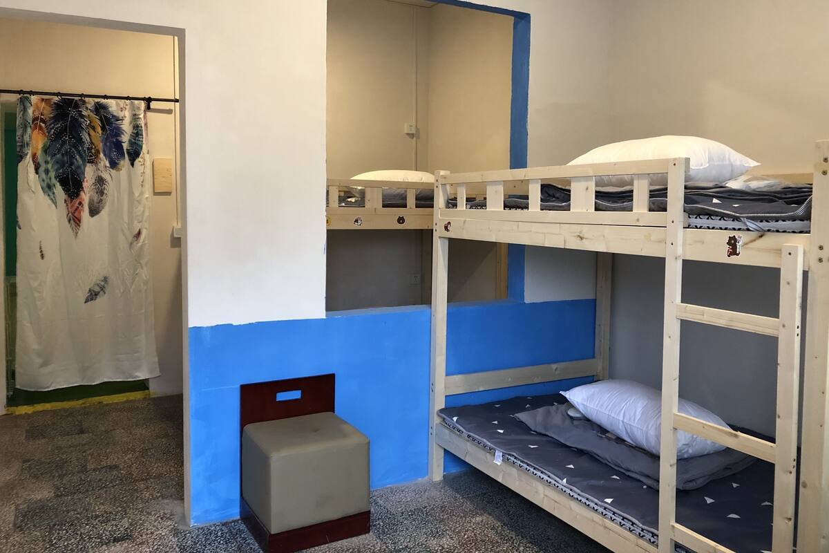 Quarto com beliche, um banquinho pequeno, um espelho e uma porta com cortina.