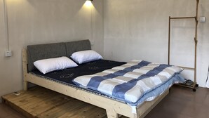 Una cama individual con estructura de madera, dos almohadas blancas y una manta azul y blanca a rayas. Hay dos lámparas fijadas a la pared a cada lado de la cama.