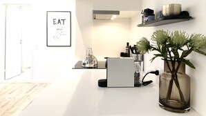 Una cocina moderna con encimera blanca, hervidor, licuadora y planta en jarra de cristal.