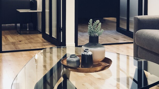 Una habitación moderna con una mesa de centro de vidrio, un sofá y una cama con vistas a través de amplios ventanales.