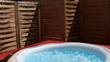 An outdoor hot tub with a red deck, surrounded by wooden fences, under a clear blue sky.